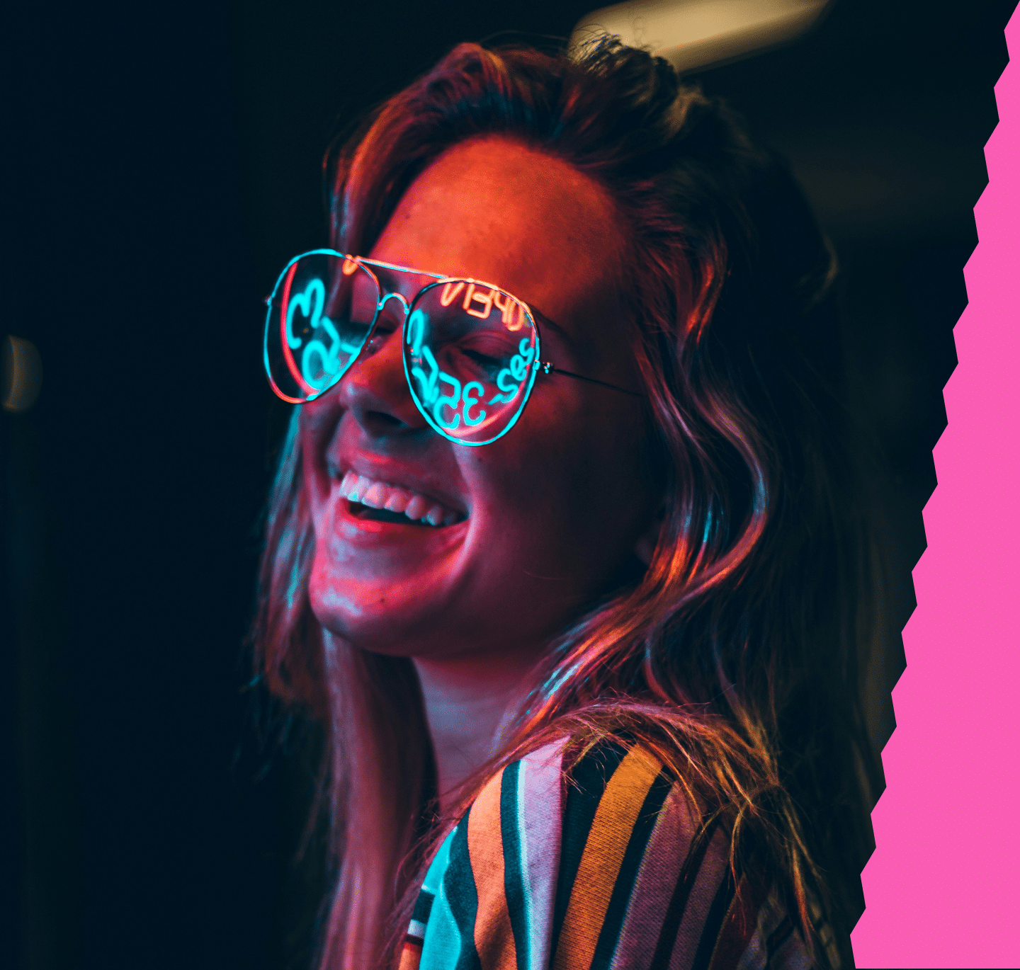 A smiling woman in aviator sunglasses, reflecting "OPEN 24/7" in neon blue, is lit by red light.