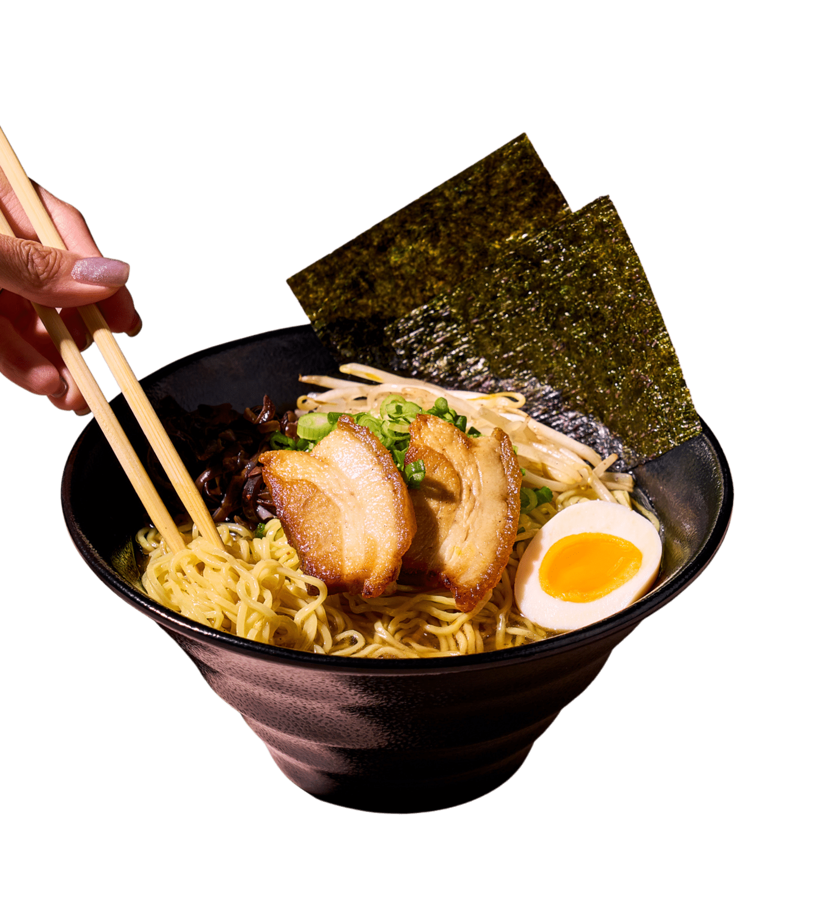 A hand uses chopsticks to pick up noodles from a black bowl of ramen with pork, egg, and seaweed.